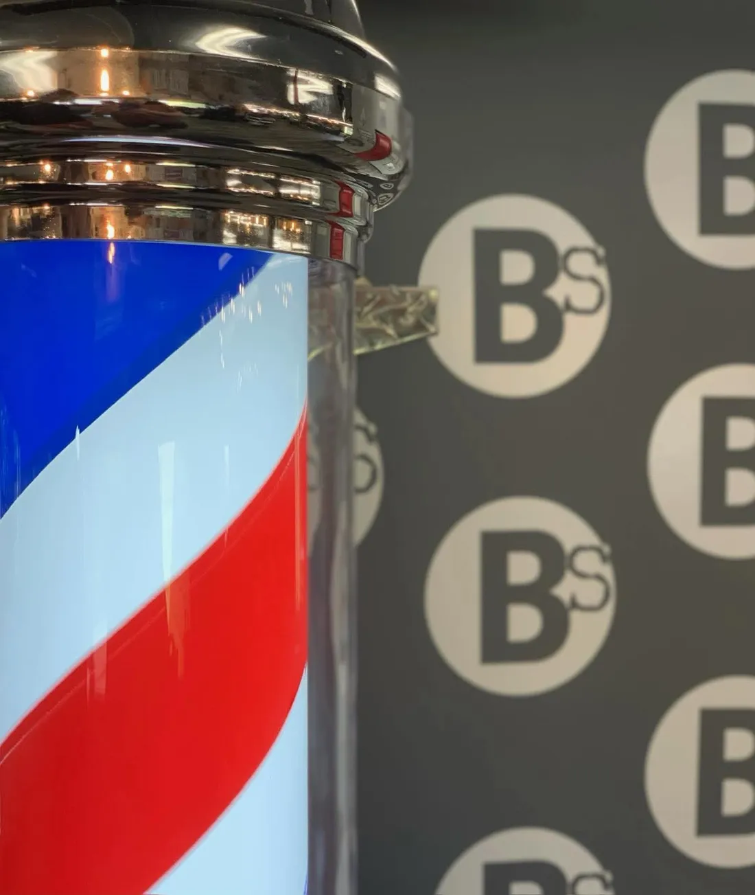 A classic barber pole beside the Barber Shack BS logo wall in Bellingham.