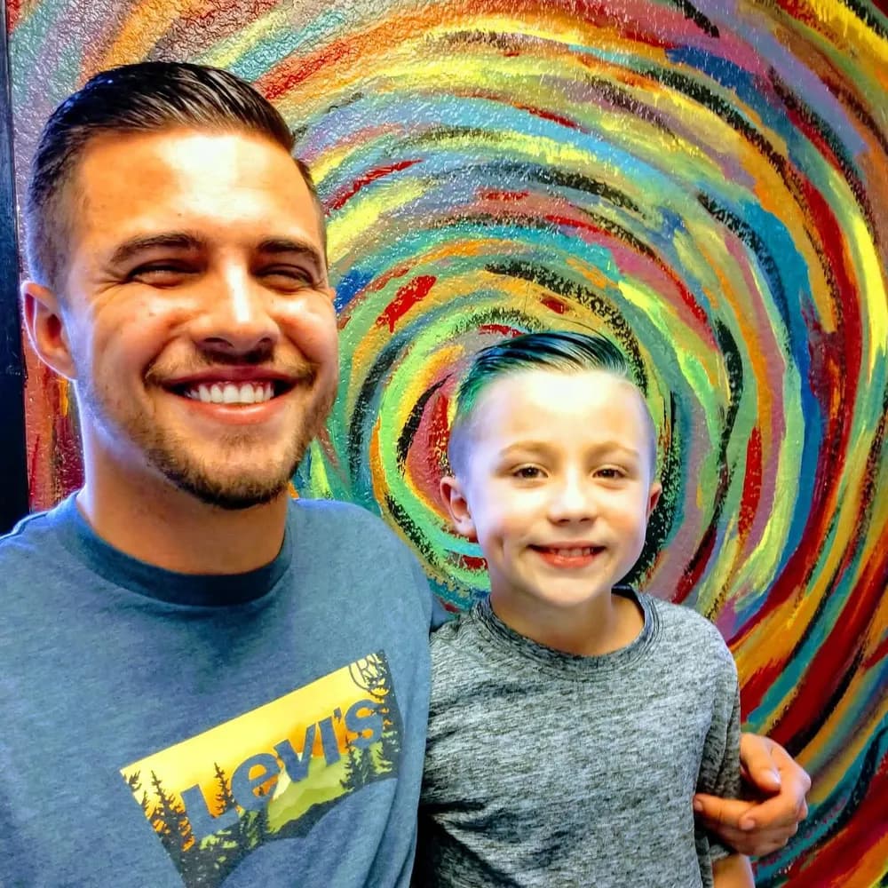 A client and his son in front of the Barber Shack community art wall.