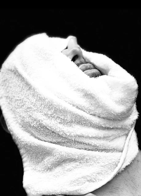 A hot towel wrapped and steaming before a straight-razor shave, in black and white.