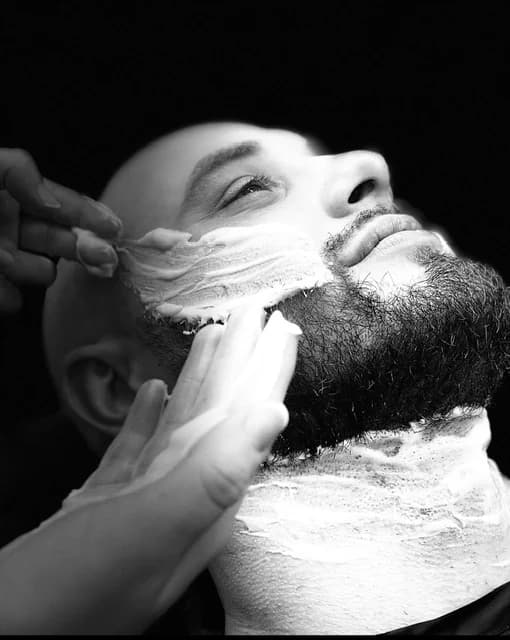 A straight razor working through the lather along a client's jaw, in black and white.